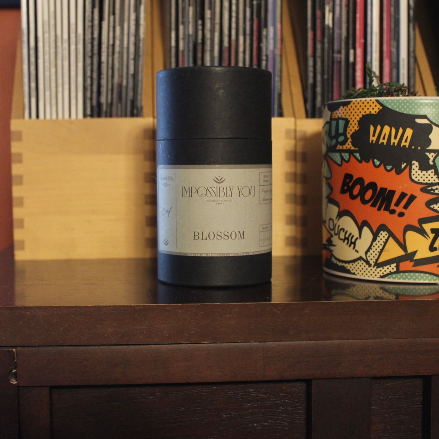 Blossom scented Impossibly You wax melts on a shelf next a planter and magazines.