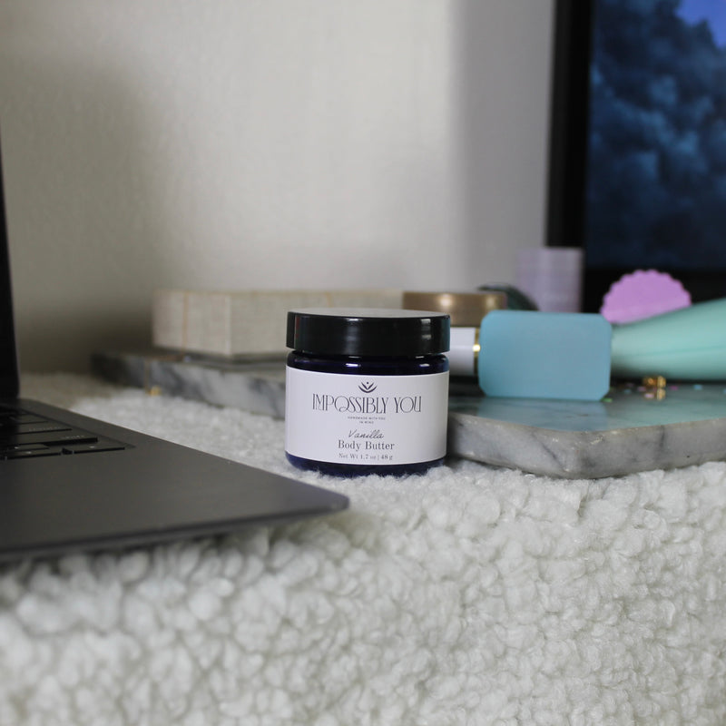 impossibly you vanilla scented 2 oz body butter next to a laptop and marble tray.