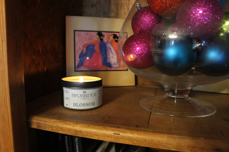 scented soy wax candle sitting on a shelf with art work and a vase of christmas ornaments
